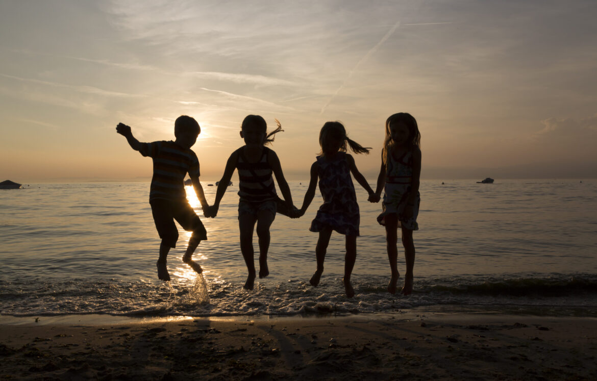 Italy, Lake Garda, children jumping on beach at sunset