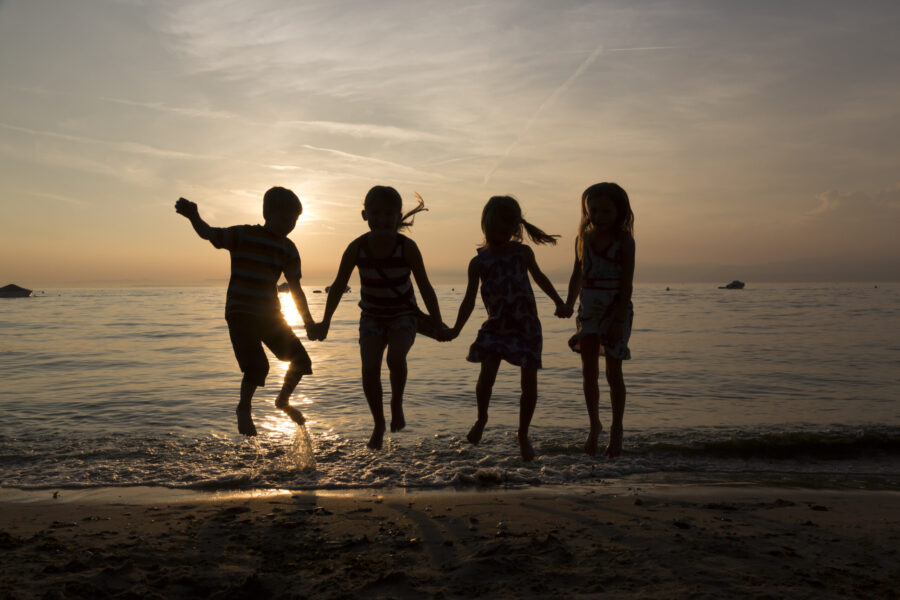 Italy, Lake Garda, children jumping on beach at sunset